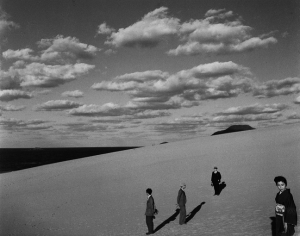 「妻のいる砂丘風景（3）」（1950年）です。鳥取砂丘を舞台に、作者の妻と仲間たちがいろんな方向を向いて立っている様子をとらえた白黒写真です。